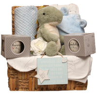 Baby boy hamper with Tommy the dinosaur toy, blue blanket, baby clothing and parent mugs in a wicker basket