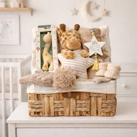Luxury giraffe baby gift hamper in neutral nursery with plush toy, rubber teether, knitted blanket and newborn baby essentials in wicker basket.