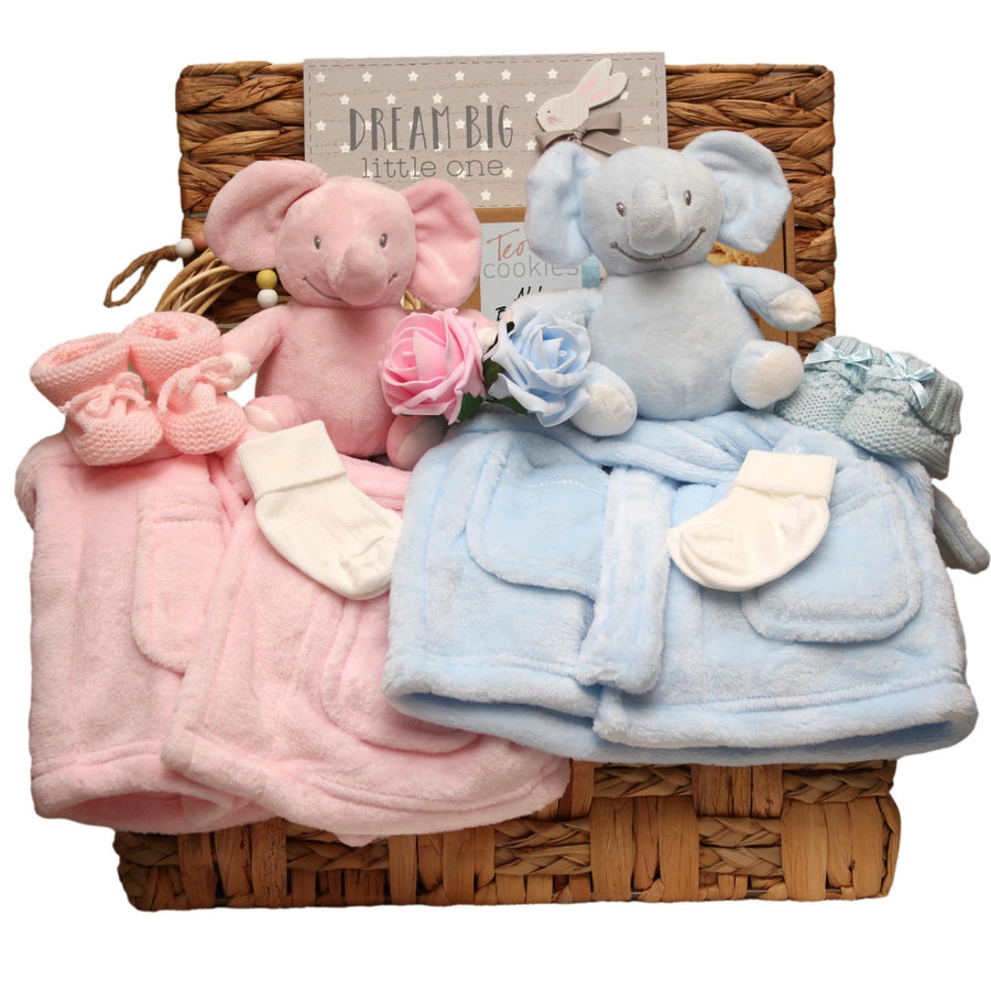 Baby twins gift set with plush elephant toys in blue and pink, matching dressing gowns and a 'Dream Big Little One' sign arranged in a basket. 