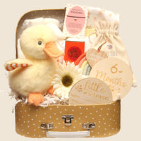 A yellow polka dot suitcase gift hamper filled with a soft plush duck toy, wooden milestone discs, a “Precious Little One” rainbow decoration, a cream baby blanket, a small gift pouch, a daisy flower, and a bracelet for a new mum.